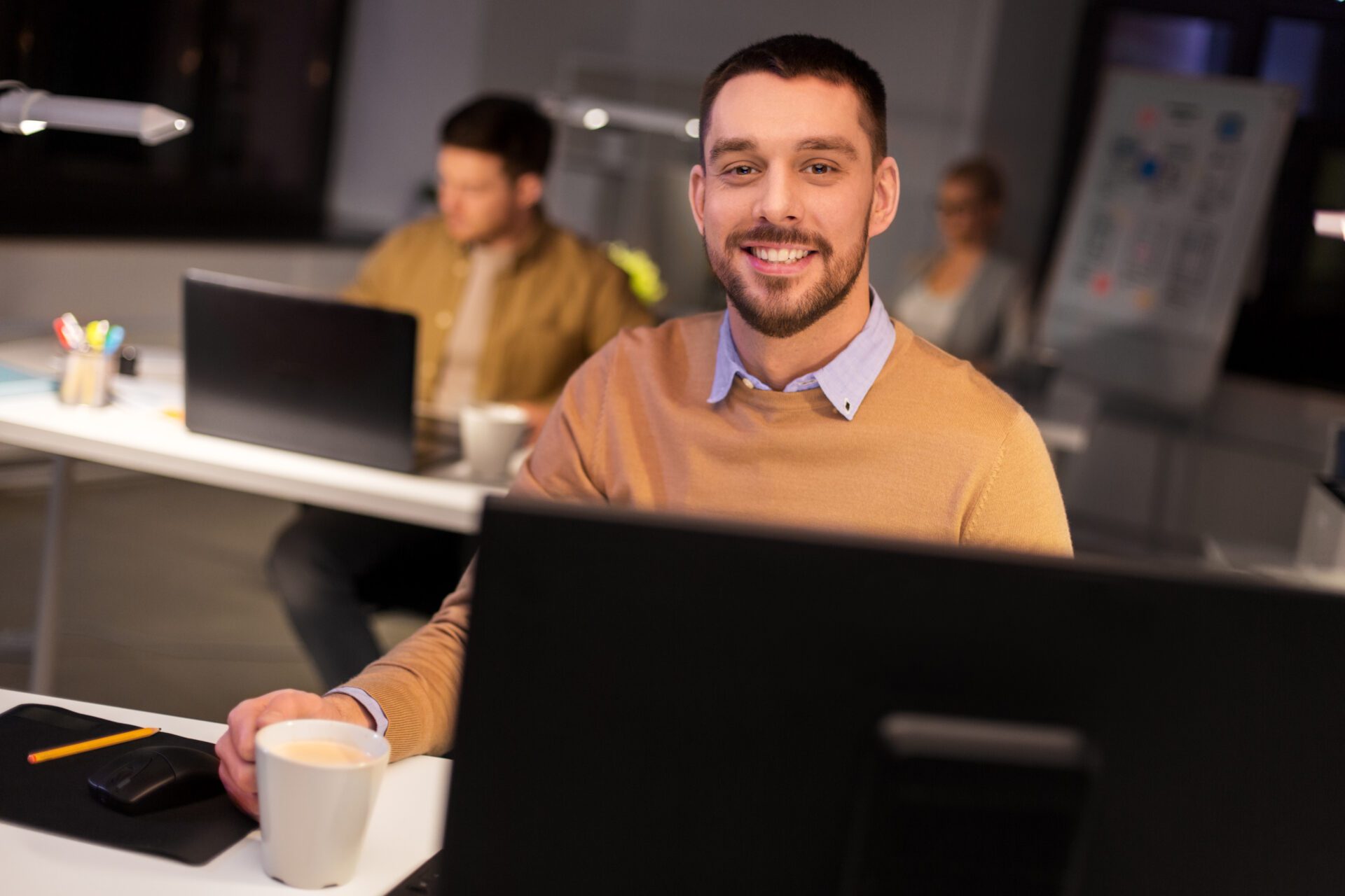 happy male office worker drinking coffee technician smiling with a mug work on a computer